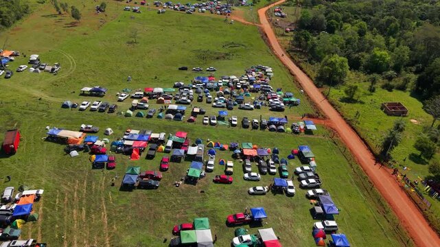 Aerial Dolly View of Rally Campsite in Nueva Alborada Paraguay with Red Dirt Road and Parked Cars