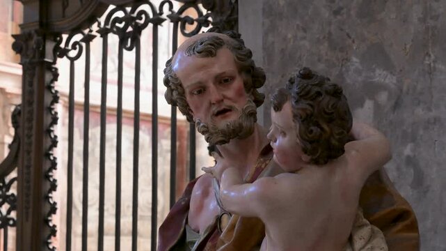 Close view of a painted religious statue of a bearded saint holding a child inside Naples Cathedral, lit softly against stone walls and ironwork.