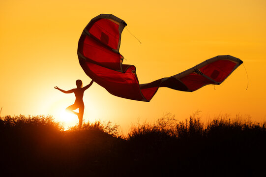 Silhouette Of Woman Doing Yoga Pose With Kite At Sunset