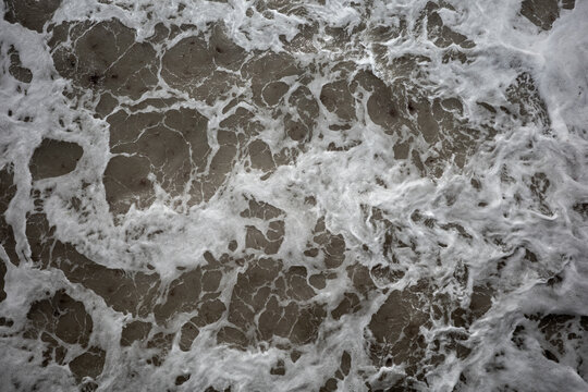 Waves crashing on the shore create a pattern in the sand at a beach during the daytime