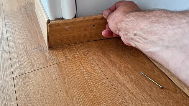Fitting a wooden baseboard into a floor corner, aligning the trim against the wall and laminate flooring during home renovation and interior finishing work