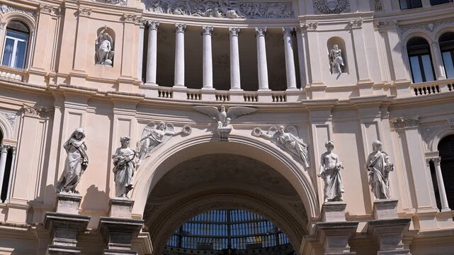 Classical marble statues and ornate reliefs frame the main entrance arch of Galleria Umberto I in Naples under bright daylight.
