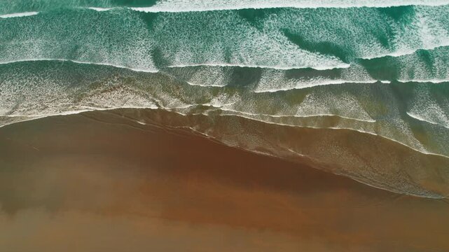 Aerial view of ocean waves meeting dark sandy beach