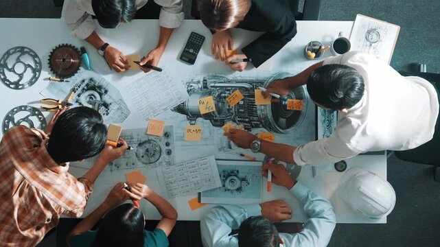 Top view of smart engineer team in casual cloth talking about turbine engine structure at table with metal gear, calculator, sticky notes. Group of technician taking a note in meeting. Alimentation.