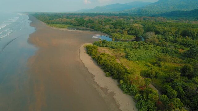 Wide sandy beach meeting green forest and mountains in tropical Costa Rica