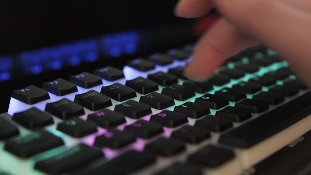 Woman hand typing on computer keyboard with neon backlight in dark office room close-up