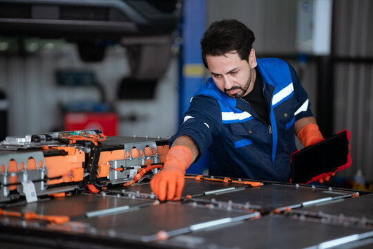 Electric vehicle technician performing battery repair in modern automotive shop with tools and equipment