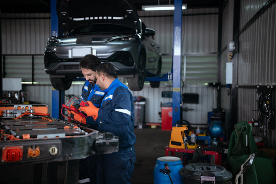 Two technicians are inspecting an electric vehicle battery in a repair shop.