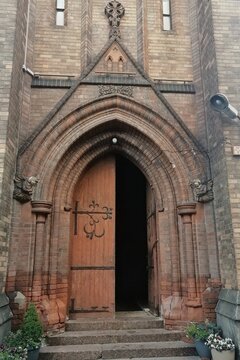 Ancient wooden portal with forged metal hinges and stone carved angels on a brick building facade