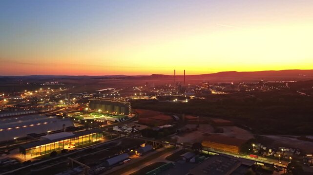 An industrial area during sunset. Factories and power plants are visible. The sky is filled with colors as lights turn on in the buildings.