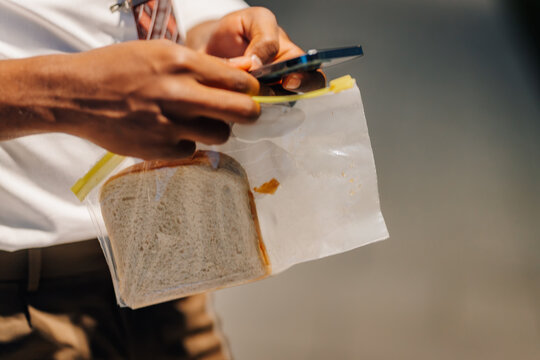 Person holding sandwich in plastic bag and phone