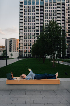 Woman relaxing on bench checking smartphone in urban park