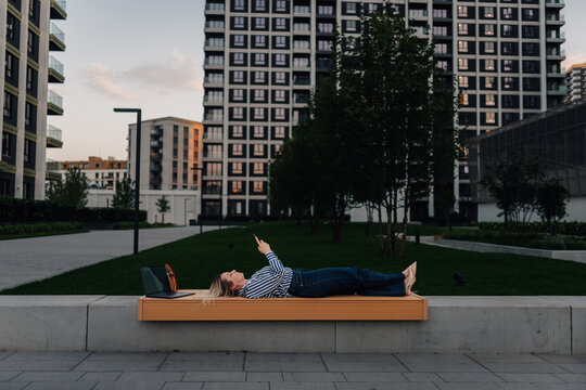 Woman relaxing outdoors with smartphone and laptop