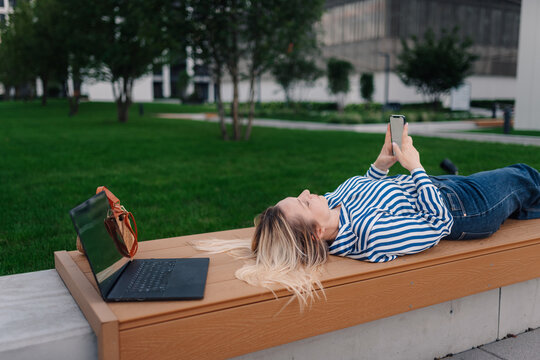 Woman relaxing on park bench checking smartphone