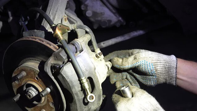 Mechanic connects a new hydraulic brake hose to car caliper.