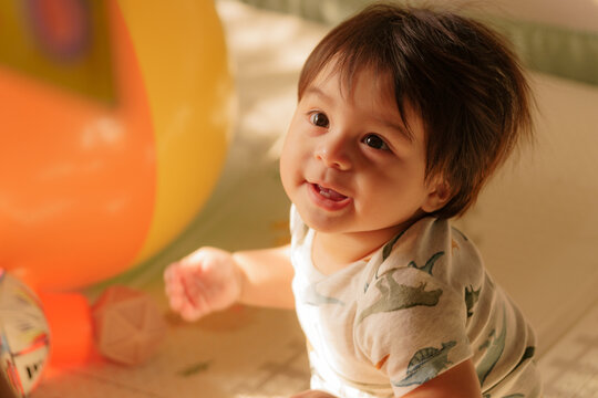 Smiling baby playing beside colorful balloons at home in warm natural light, capturing a joyful moment of childhood, curiosity and celebration.