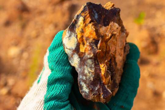 Stunning raw flint stone with chalcedony inclusions held by a gloved hand against a sandy quarry background, showcasing natural patterns and beautiful earthy textures of geological treasures