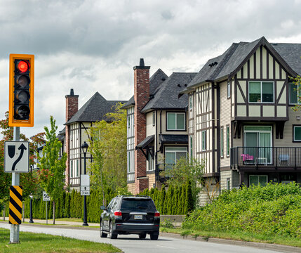 A suburban street past Tudor-style townhouses with black SUV on the road and a red traffic light