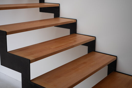 Modern indoor staircase with wooden treads and solid black steel plate stringers made from continuous thick metal sheets, set against clean white walls.