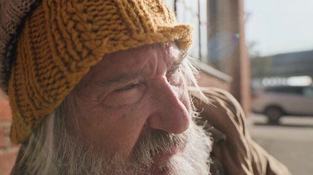 Senior Caucasian homeless man rubbing face while sitting outdoors on street sidewalk. Ideal for social welfare campaigns, poverty awareness videos, charity projects, and nonprofit advocacy