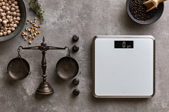 Digital kitchen scale and vintage balance scale with chickpeas and pepper on rustic grey background.