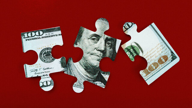 Puzzle pieces made from dollar bills on a red background showing parts of a hundred dollar note