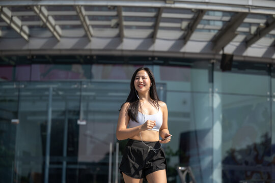 Young Asian woman runner jogging outdoors near modern glass building in city