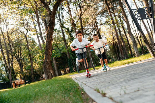 Two boys ride scooters in a park during daytime enjoying outdoor activity
