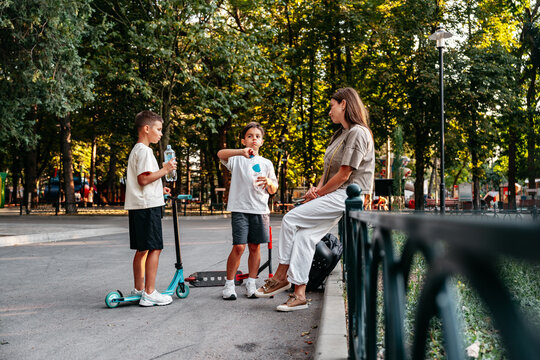 Two children talk and enjoy snacks with a woman in a park during daytime