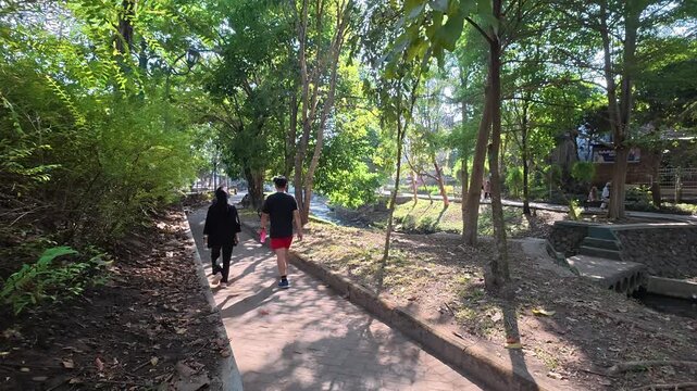 People walking along shaded pathway through lush green park