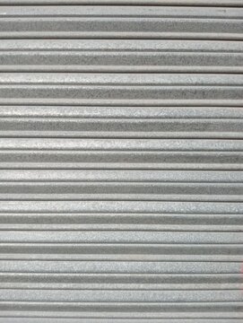 Corrugated metal sheet texture photograph. Horizontal parallel grey steel lines and ribbed pattern surface. Industrial background for architecture, construction, and design projects.