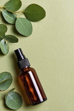 Brown glass bottle with black spray nozzle sits beside green leaves