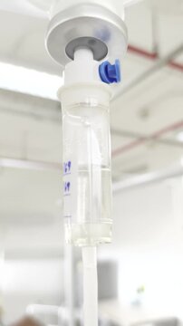 Close-up of IV drip chamber dripping saline solution in a hospital room