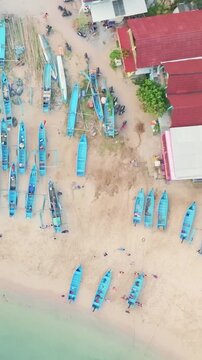High aerial view shows numerous blue fishing boats spread across a sandy tropical beach beside turquoise water.