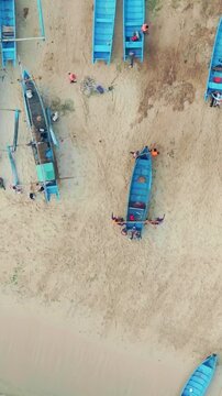 Top-down aerial view of blue fishing boats and local activity along a wide sandy tropical beach in Indonesia.