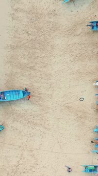 Overhead aerial view of fishermen gathered around a colorful blue boat resting on a broad sandy beach.
