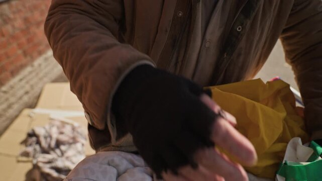 Senior Caucasian man searching through bags and coughing outdoors. Footage suitable for social awareness campaigns, charity foundations, and poverty documentary storytelling