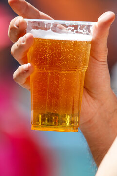 Hand holds clear plastic cup with golden beer and foam