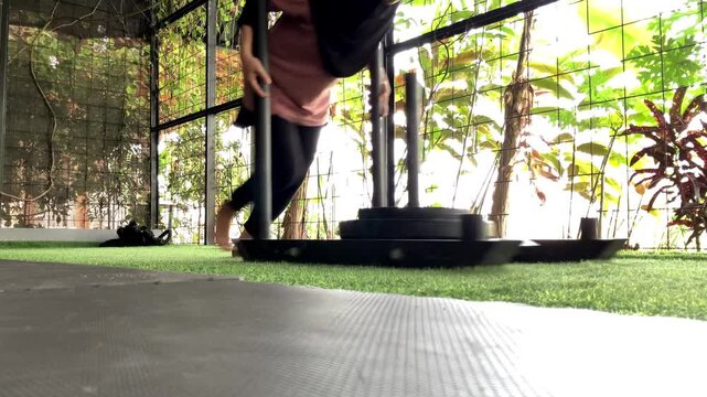 Slow motion video of a hijab-wearing woman pushing a heavy weight sled on artificial turf during a functional strength and conditioning workout in a modern gym.