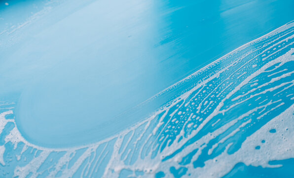 Blue surface with a broad wiped area and diagonal foam edge during household cleaning.