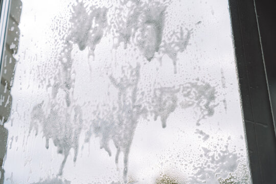 Large patches of cleaning foam dripping down a window against a cloudy sky.