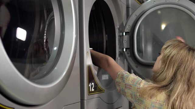 Close-up of a beautiful woman taking out a clean and dry shirt from the dryer or washing machine. The process of working at a self-service laundry.