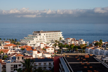 A stepped white hotel stands at the water edge among terracotta roofed apartments. A thick band of cloud sits along the horizon over the Atlantic at Los Gigantes. © Oksana