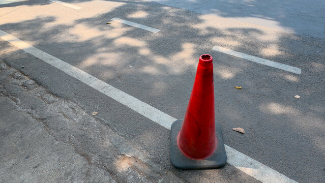 Orange traffic cone standing on shaded asphalt road