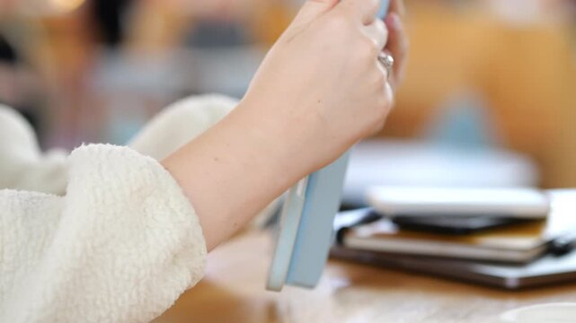 Close-up of hands holding and using a tablet. Person wears cozy white sweater. Fingers tap screen, focused on device. Blurred background shows indoor space