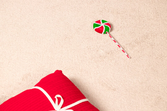 Festive Christmas lollipop and a wrapped red gift box on a soft textured neutral background