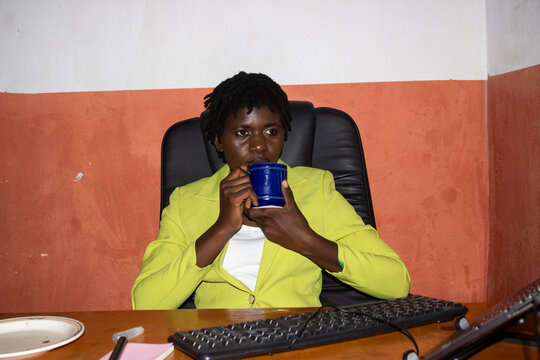 Black woman holding blue mug at wooden desk in Blantyre office, Malawi &mdash; eye-level portrait of focused professional