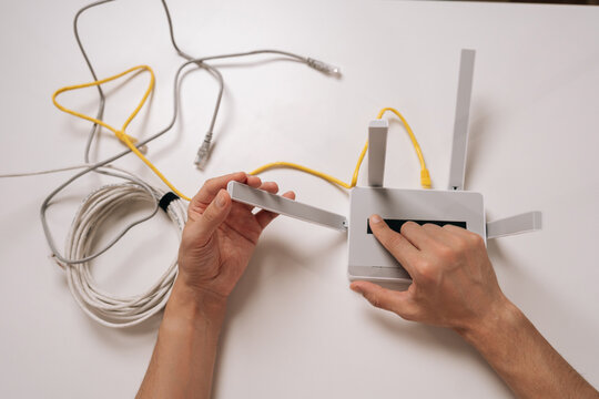 High-angle view of technician connecting an ethernet cable to a white wireless router, establishing internet connection for home or office network setup and technology support.