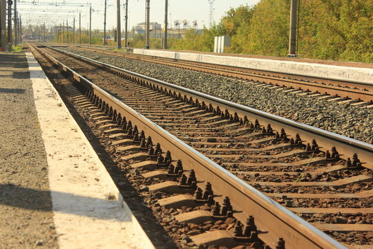 Perspective view of parallel railway tracks near a station platform on a sunny day