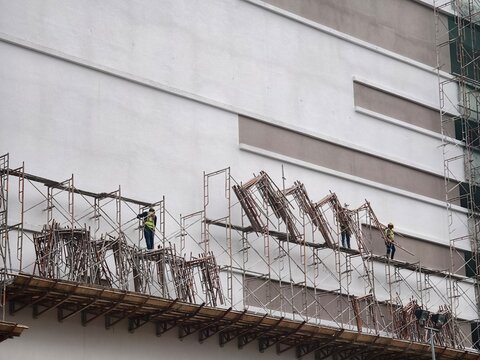 Construction workers on a high scaffolding structure installing exterior cladding panels on a modern building facade. Industrial civil engineering, real estate development, and workplace safety concep